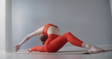 Kırmızı spor eşofmanlı genç bir kadın sicimin üzerine oturur ve ağır çekimde ileri geri eğilir, beden eğitimi, esneme ve jimnastik yapar, 4k 120p Prores karargahı 10 bit