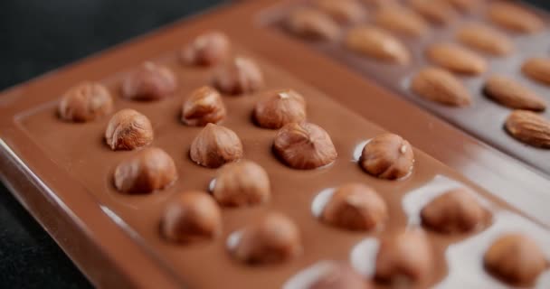 Pan shot: czekolada bar z orzechami laskowymi kładzie w formie silikonu, sztuka wytwarzania ręcznie robionej czekolady, naturalne desery z czekolady i kakao, cukierki czekoladowe, 4k 120 fps Prores HQ — Wideo stockowe