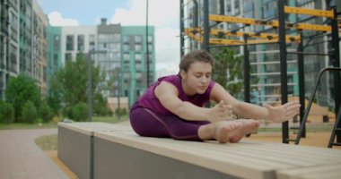 Kadın bir apartmanın bahçesindeki bankta esneme ve yoga egzersizleri yapıyor, şehir ortamında fitness, yoga sınıfı açık havada, şehirde fiziksel egzersiz, 4k 120p Prores HQ
