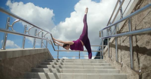 Sportowa kobieta wykonuje ćwiczenia rozciągające na poręczach schodów ulicznych, fitness w środowisku miejskim, zajęcia jogi na świeżym powietrzu, trening fizyczny w mieście, 4k 120p Prores HQ — Wideo stockowe