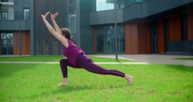 Atletik kadın apartman kompleksinin yakınındaki çimlerde spor yapıyor, şehir ortamında spor yapıyor, yoga sınıfında açık havada, şehirde fiziksel antrenman yapıyor, 4k 120 peni Prores genel merkezi.