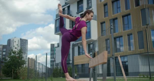 Mujer atlética hace torzal vertical de pie en el banco, ejercicios de estiramiento en el entorno urbano, clases de yoga al aire libre, entrenamiento físico y fitness en la ciudad, 4k 120p HQ de Prores — Vídeos de Stock