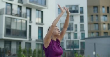 Genç kadın eller ve omuzlar için esneme egzersizleri yapıyor, apartmanın bahçesinde ısınma egzersizleri, şehir ortamında yoga dersleri, şehirde fiziksel egzersiz ve fitness yapıyor.