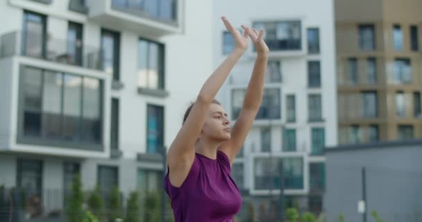 Giovane donna fa esercizi di stretching per mani e spalle, allenamento di riscaldamento nel cortile di un condominio, lezione di yoga in ambiente urbano, allenamento fisico e fitness in città — Video Stock