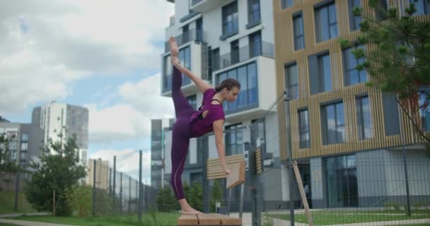 Спортивная женщина делает вертикальную бечевку стоя на скамейке, упражнения на растяжку в городской среде, йога класс на открытом воздухе, физические тренировки и фитнес в городе, 4k 120p Прорес HQ — стоковое видео