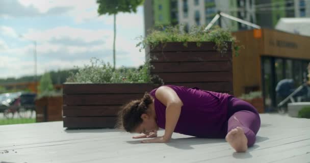 Atletische vrouw zit op een touw op de bank en doet dends vooruit, stretching in de tuin van een appartementencomplex, fitness in de stedelijke omgeving, yoga buiten, fysieke training in de stad — Stockvideo