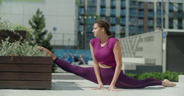 Atletisk kvinna gör garn på en offentlig gård, sträcker sig i stadsmiljö, yoga klass utomhus i slow motion, fysisk träning och fitness i staden, 4k 120p Prores HQ — Stockvideo