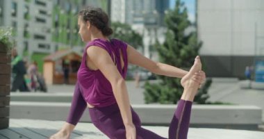 Atletik kadın sicimin üzerine oturur ve bahçeye uzanır, şehir ortamında spor, yoga sınıfı açık havada, şehirde fiziksel antrenman, yaz günü antrenman.