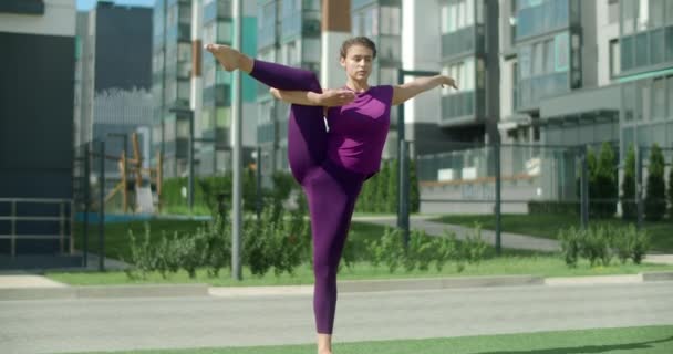Atletisk kvinde står på det ene ben og gør strækøvelser, opvarmningstræning i beboelsesområdet, fitness i bymiljøet, yoga klasse udendørs, fysisk træning, 4k 60p Prores HQ – Stock-video