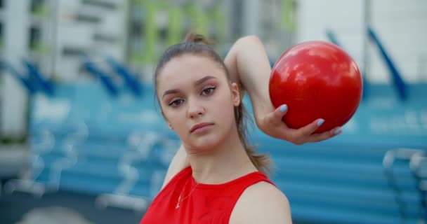 Portrét ženy v červeném sportovním kostýmu provedení kallisthenické cvičení s gymnastickým míčkem venku, sport v městském prostředí, gymnastika ve městě, 4k 120p Prores HQ — Stock video
