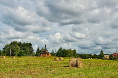 Arka planda saman balyaları ve ahşap kilise ile Yaz kırsal peyzaj