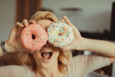 Güneş gözlüklü gülümseyen sarışın ikizler donut yiyor ve pembe arka planda kapalı gözlerle eğleniyor, hızlı ayak, tatlı pasta, krep, turta, hipster portresi,