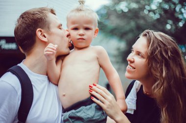Mutlu aile tatilleri. Neşeli baba, anne, bebek gün batımının kıyısında siyah kumsalda sörf yaparak eğleniyor. Aktif ebeveynler ve insanlar yaz tatillerinde çocuklarla dışarıda etkinlik yapıyorlar..