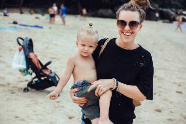 Anne ve oğlu gün batımında parkta oynuyorlar. İnsanlar sahada eğleniyor. Arkadaş canlısı aile kavramı ve yaz tatili.