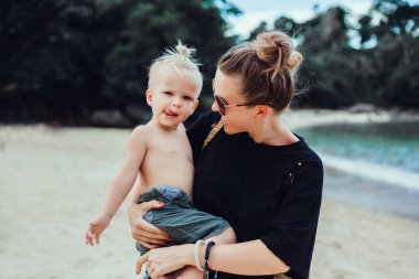 Anne ve oğlu gün batımında parkta oynuyorlar. İnsanlar sahada eğleniyor. Arkadaş canlısı aile kavramı ve yaz tatili.