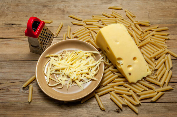 red grater, palte of cheese, hard pasta on a light, old wooden board