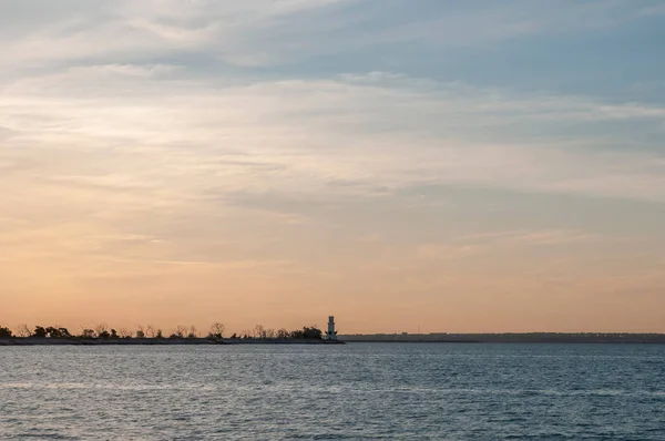 Yellow sky and a distant lighthouse on a dam at sunset — Stock Photo, Image