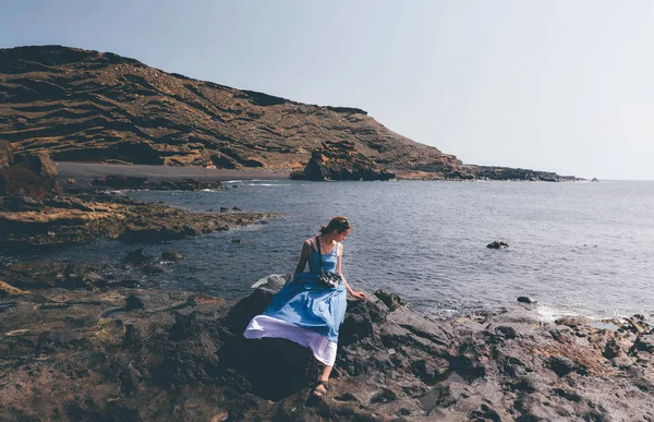 Kvinna sittande på klippstrand och avkopplande vid solnedgång. Royaltyfria Stockbilder