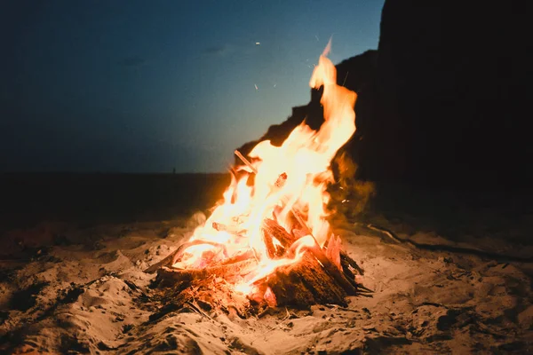 夏日阳光明媚的夜晚,沙滩上的火苗熊熊燃烧.在空旷的海滩上的壁炉里,篝火熊熊燃烧.带有电影和谷物效果的照片 — 图库照片