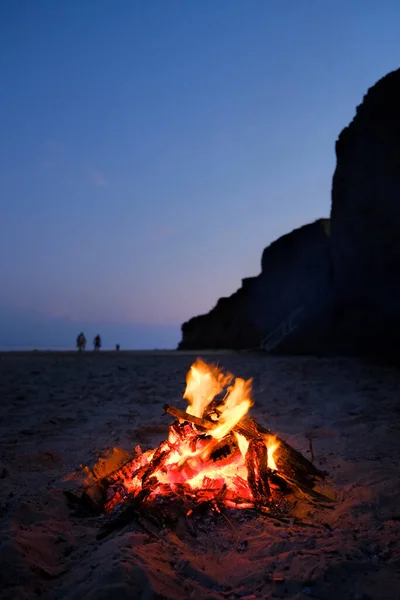 Eld brinner på sandkusten en solig sommarkväll. Liten eld brinner inne i en öppen spis på den tomma stranden vid vacker solnedgång. Stockfoto