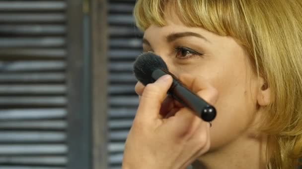 O artista de maquilagem profissional aplica o pó com a escova em uma cara de cliente. beleza indústria da moda — Vídeo de Stock