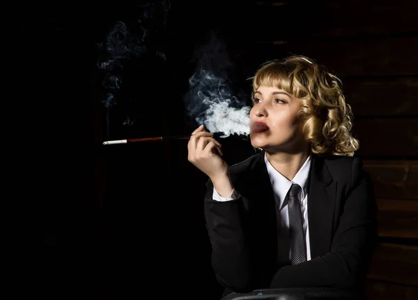 Mujer de negocios con cigarrillo sobre un fondo oscuro, retrato retro estilizado — Foto de Stock