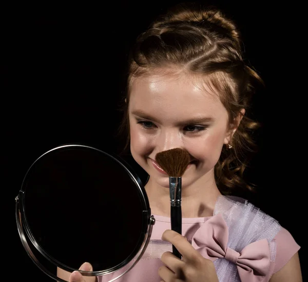Маленька дівчинка з круглим дзеркалом робить макіяж на темному тлі — стокове фото