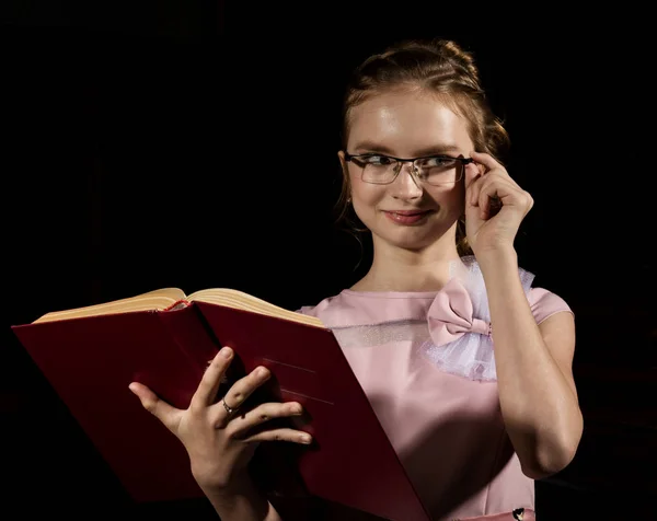 Liebliches kleines Mädchen steht und liest Buch vor dunklem Hintergrund — Stockfoto