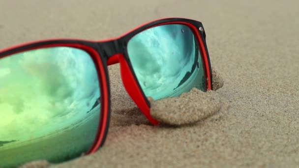 Sunglasses lying on the sand. In a sunglasses reflected sea, waves and sky. — Stock Video