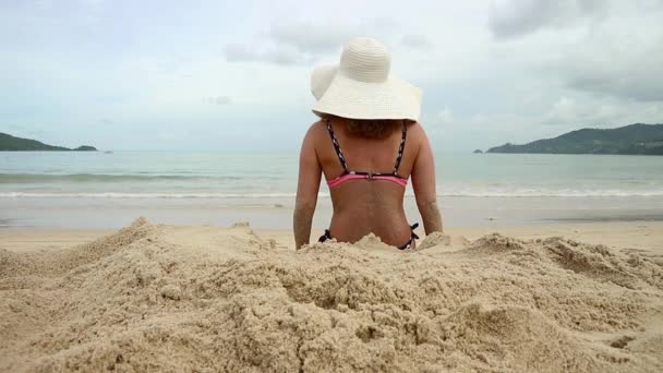 Leuke vrouw in een witte breed-rand rustend op een zonnige zandstrand — Stockvideo