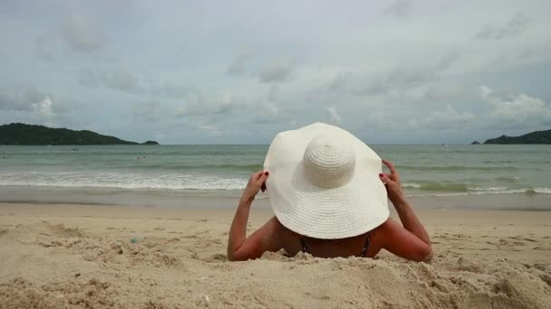 Симпатична жінка в білому широкому пляжі відпочиває на сонячному піщаному пляжі — стокове відео
