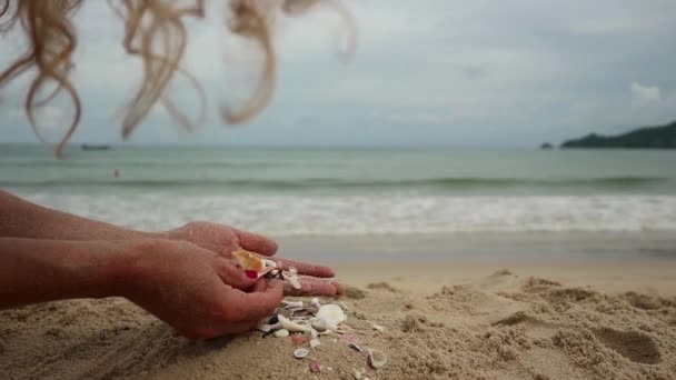 Frauenhände spielen mit Sand am exotischen Strand und vor verschwommener Meereskulisse. Sommerferienkonzept — Stockvideo