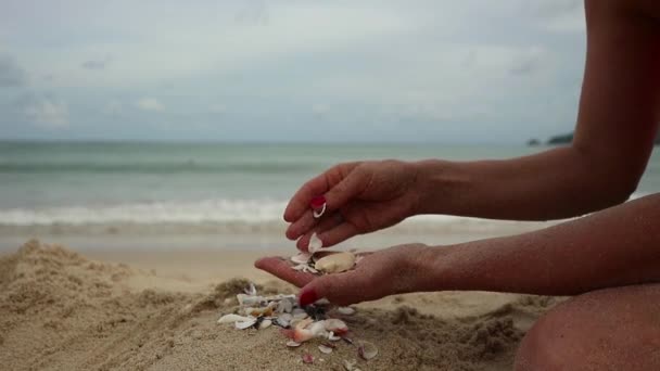 Frauenhände spielen mit Sand am exotischen Strand und vor verschwommener Meereskulisse. Sommerferienkonzept — Stockvideo