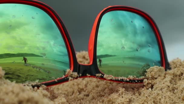 Solglasögon liggande i sanden på en strand. I en solglasögon återspeglas hav, vågor och himmel. — Stockvideo