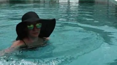 Genç kadın siyah geniş ağzına kadar ve yüzme havuzunda dinlenme güneş gözlüğü