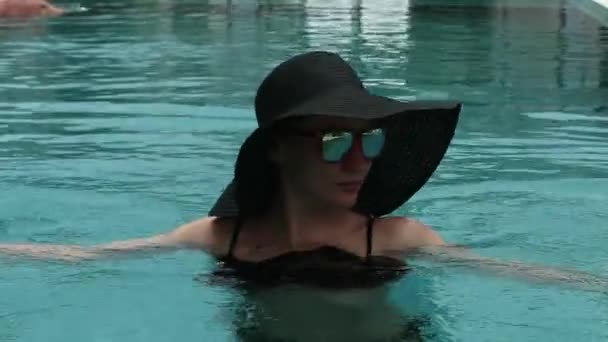 Jeune femme dans un noir large bord et des lunettes de soleil reposant dans la piscine — Video