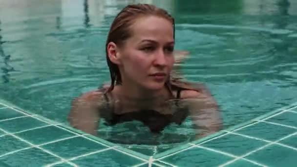 Jovem feliz bonita em óculos de sol sorrindo e relaxando na piscina do hotel — Vídeo de Stock