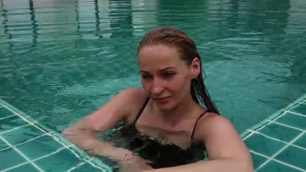 Hermosa mujer delgada feliz en un bikini negro, sonriente y relajante en la piscina del hotel — Vídeos de Stock