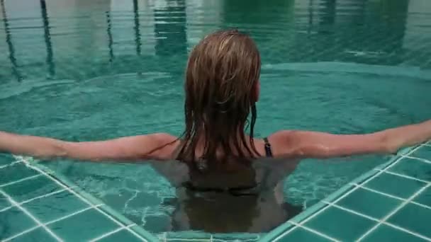 Счастливая стройная женщина в черном бикини, улыбается и расслабляется в бассейне отеля — стоковое видео