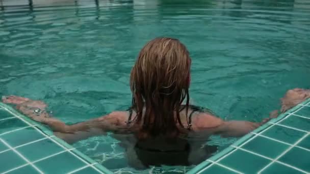 Beautiful happy slim woman in a black bikini, smiling and relaxing in hotel pool — Stock Video