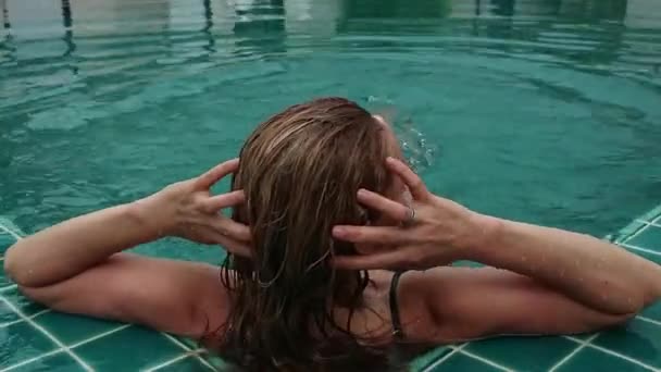 Beautiful happy slim woman in a black bikini, smiling and relaxing in hotel pool — Stock Video