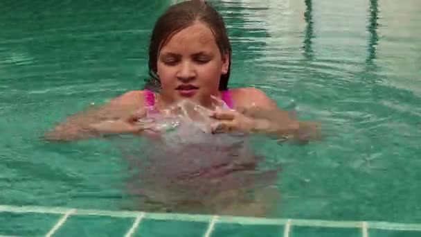 Chica jugando con el agua en una piscina del hotel. Niño divirtiéndose en el agua al aire libre — Vídeo de stock