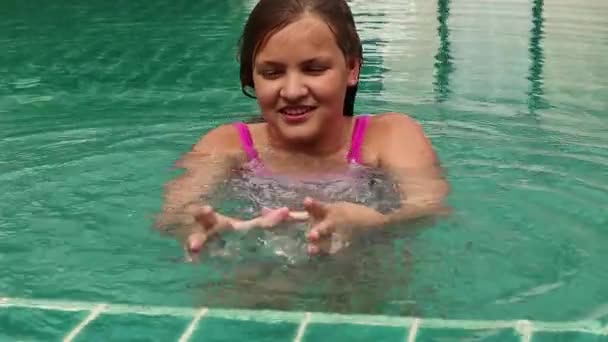 Chica jugando con el agua en una piscina del hotel. Niño divirtiéndose en el agua al aire libre — Vídeo de stock