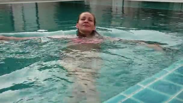 Mujer joven relajándose y nadando lentamente en la piscina — Vídeo de stock