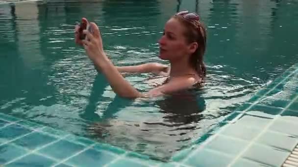 スイミング プールでリラックスの若い女性と彼女の携帯電話で写真を撮る — ストック動画