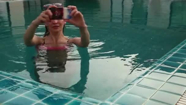 Young woman relax in swimming pool and takes pictures on her cellphone — Stock Video