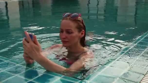 Jonge vrouw relax in zwembad en neemt foto's op haar mobiel — Stockvideo