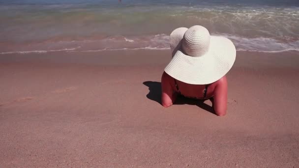 Vista trasera de la mujer en bikini y sombrero de sol blanco mientras toma el sol en la playa del paraíso de arena de mar — Vídeos de Stock