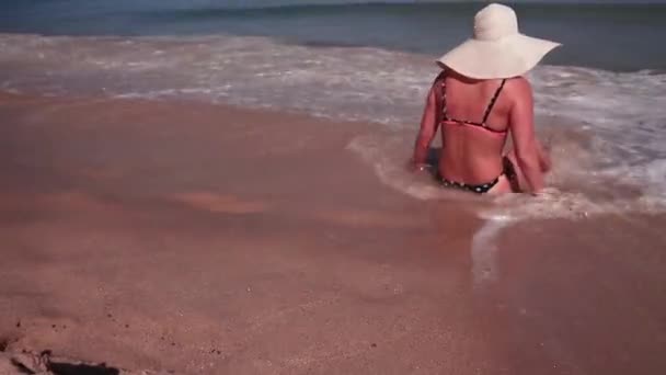 Вид сзади на женщину в бикини и шляпе белого солнца во время загара на пляже морского песка рай — стоковое видео