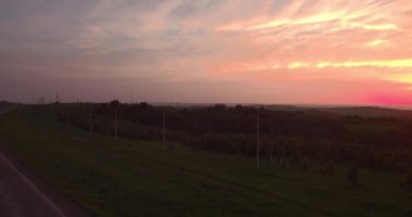 Havadan görünümü. gün batımında kırsal manzara ile yeşil tepeler geçerek uzun ve dolambaçlı yolu. 4k